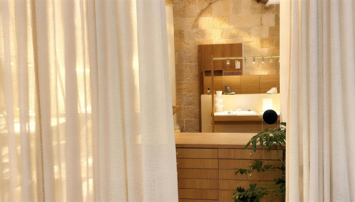Le mur de pierre et la vitrine éclairée de la boutique Atelier Paulin, vus entre deux rideaux clairs