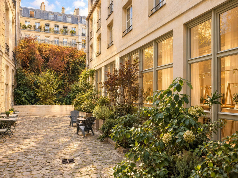 Une allée de la cour du 8 bis rue de Braque : pavés, massifs de plantes et baies vitrées éclairées de l’atelier Atelier Paulin