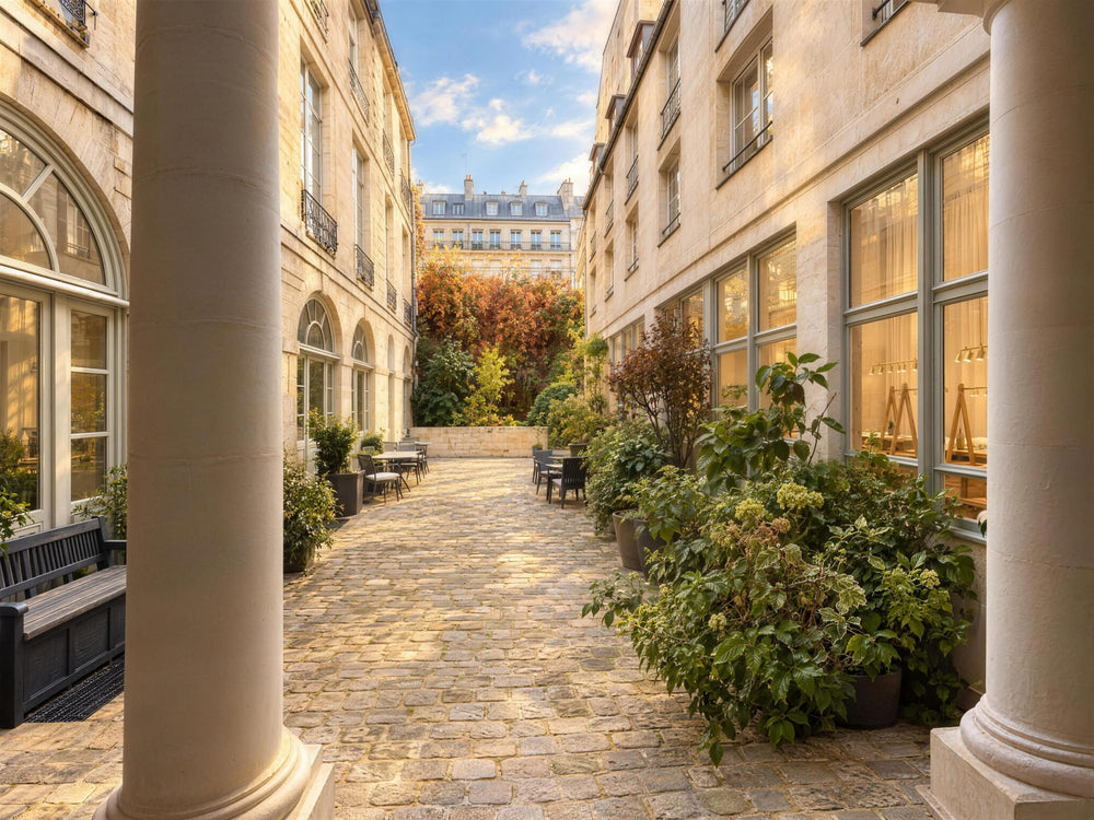 La cour du 8 bis rue de Braque vue entre deux colonnes : pavés, plantes et grandes baies vitrées de l’atelier Atelier Paulin